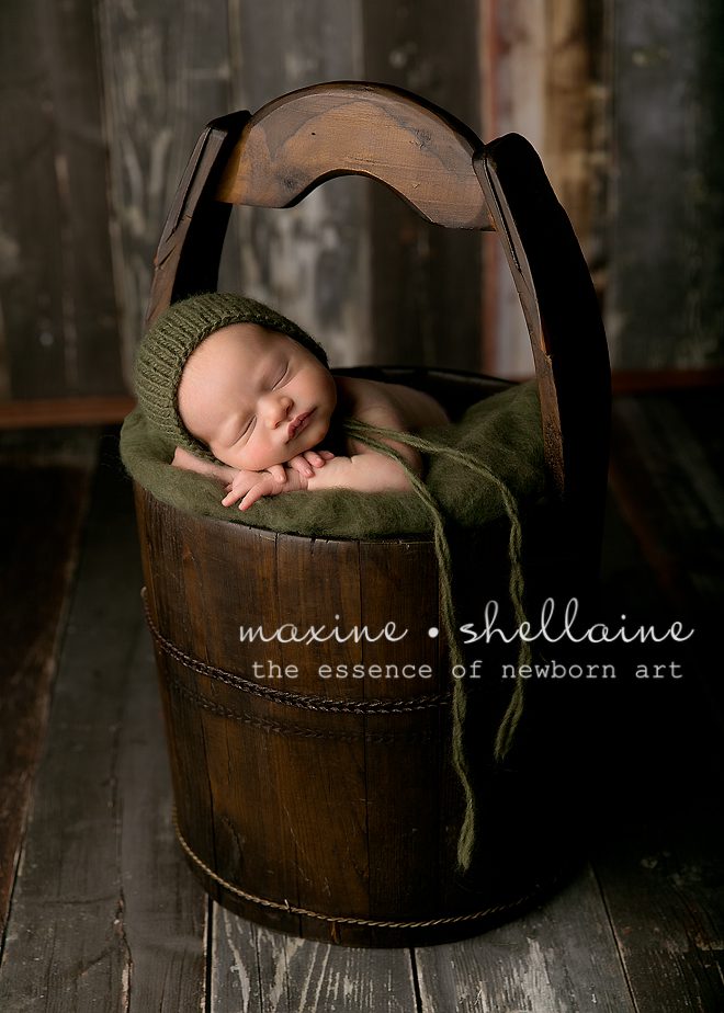 Alt=Best Newborn Photographer Edmonton, Alt=Antique Bucket Prop, Alt=dark green bonnet, Alt=wooden background, Alt=newborn baby boy, alt=posed newborn photography
