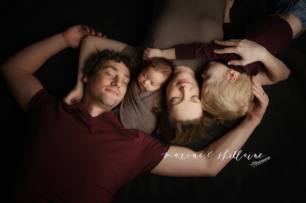 alt=Dark and moody newborn photography, alt=beautiful shadowy newborn session, alt=darker toned session, alt=dramatic lighting, alt=family lying on blanket