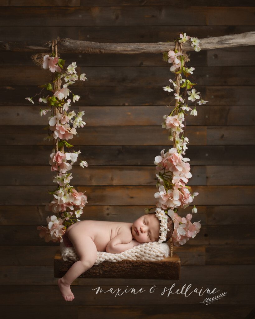 alt=baby on swing with flowers, alt=photography, alt=beautiful shadowy newborn session, alt=darker toned session, alt=dramatic lighting, alt=hanging swing shot, 