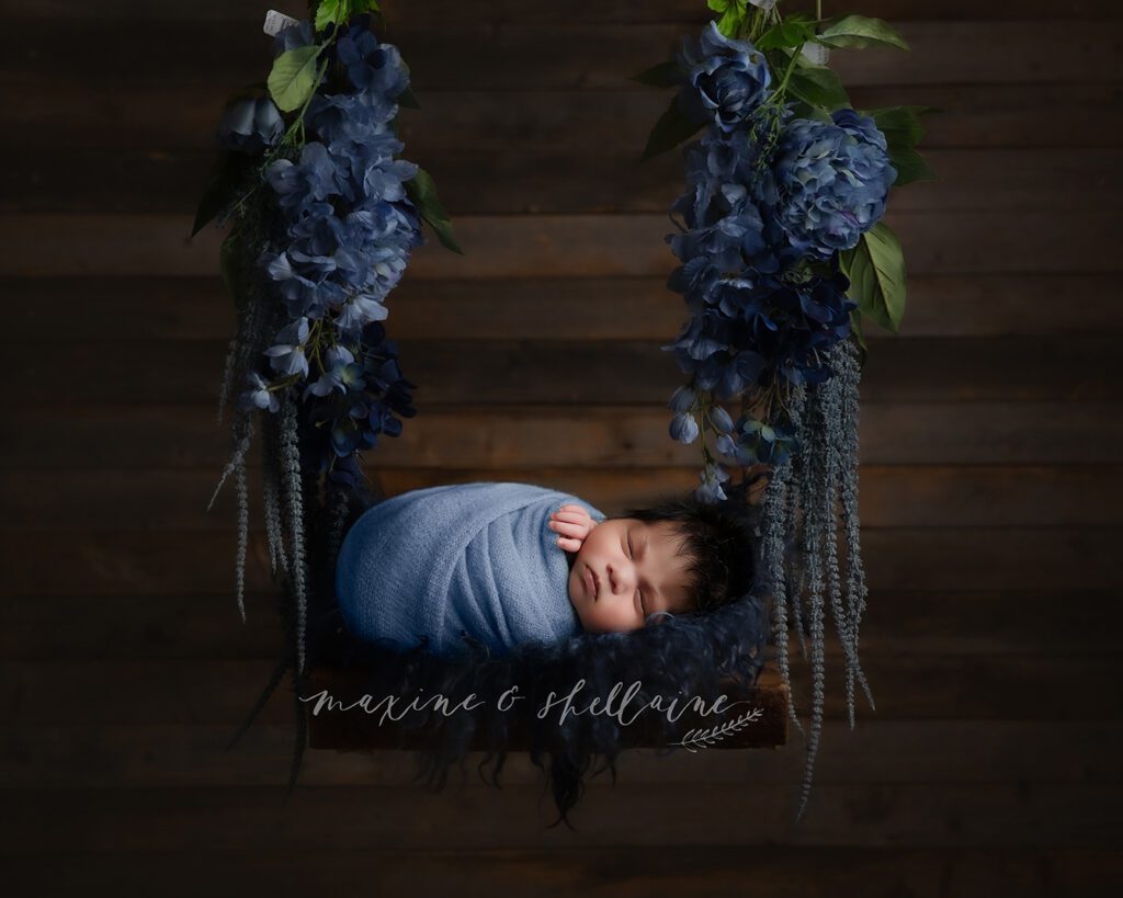 alt=Sleeping newborn baby boy on floral swing in Edmonton photography studio