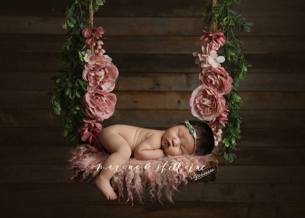 alt=Sleeping newborn baby on floral swing during Edmonton newborn photography session